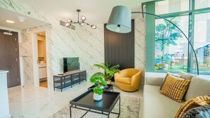 A modern living room with a marble wall, a sofa, a coffee table, and a large window with a view. - Nasma Luxury Stays - Al Raha Lofts 2 (Abu Dhabi)
