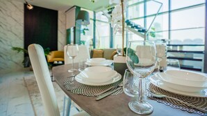 A dining table set with white plates, glasses, and cutlery, with a view of the city through large windows. - Nasma Luxury Stays - Al Raha Lofts 2 (Abu Dhabi)