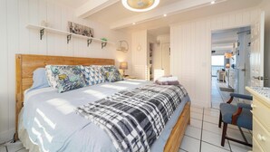 A bedroom with a wooden bed, a bedside table, a chair, and a hanging light fixture. - Beachers 421: stunning oceanfront, steps to pool, pet friendly. (St. Augustine)