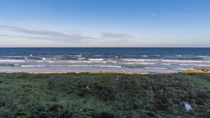 A coastal landscape with a beach, grassy dunes, and a wooden pier extending into the water. - Beachers 421: stunning oceanfront, steps to pool, pet friendly. (St. Augustine)