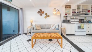 A modern living room with a sofa, wooden coffee table, and a kitchen area with white cabinets and appliances. - Beachers 421: stunning oceanfront, steps to pool, pet friendly. (St. Augustine)