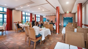 A restaurant with tables and chairs, large windows, and red pillars. - Hotel am Park (Hueckelhoven)