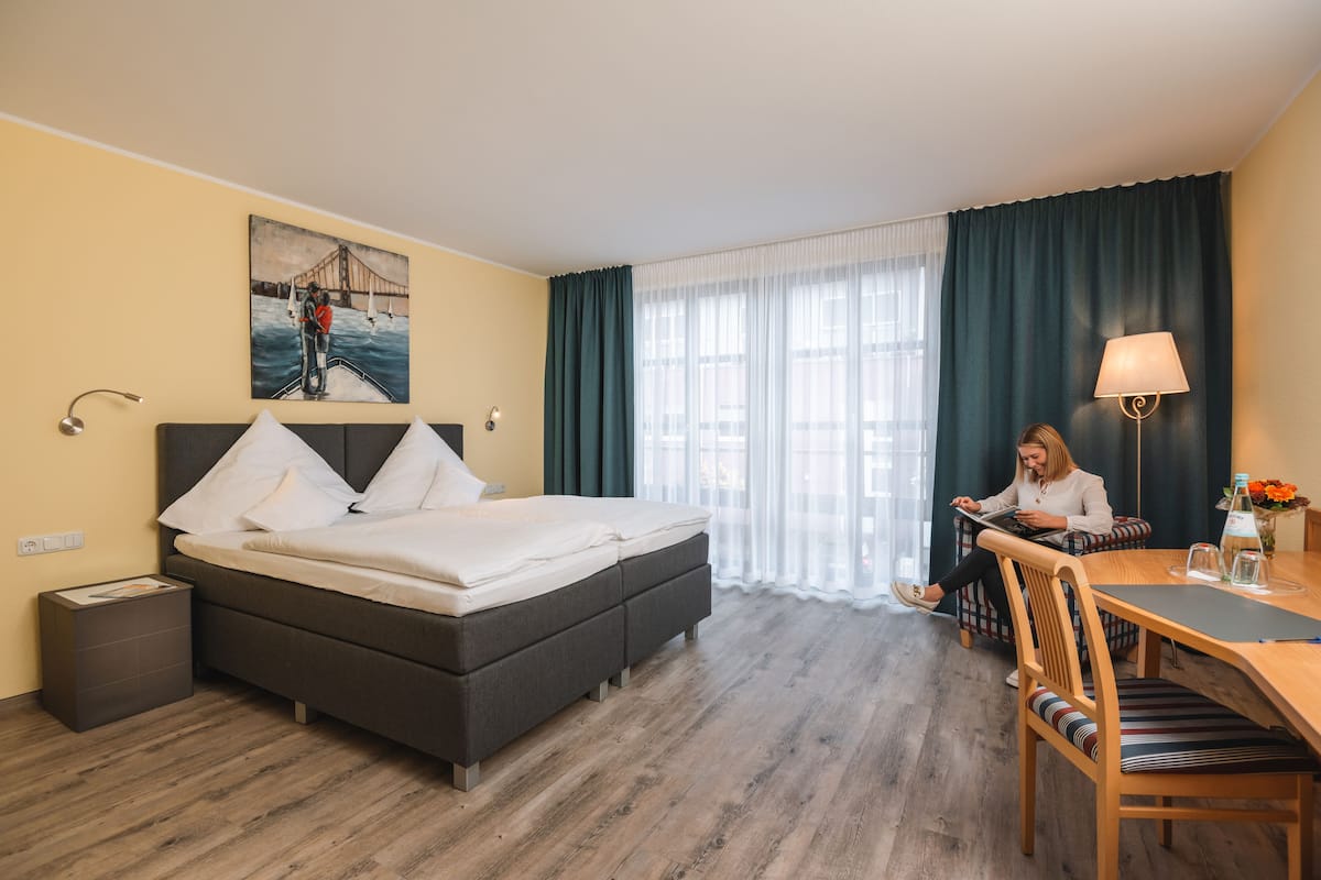 A hotel room with a bed, a desk, a chair, a lamp, and a painting on the wall.