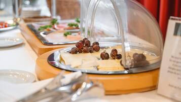 Een buffetopstelling met diverse etenswaren onder een glazen koepel, waaronder kaas, crackers en druiven.