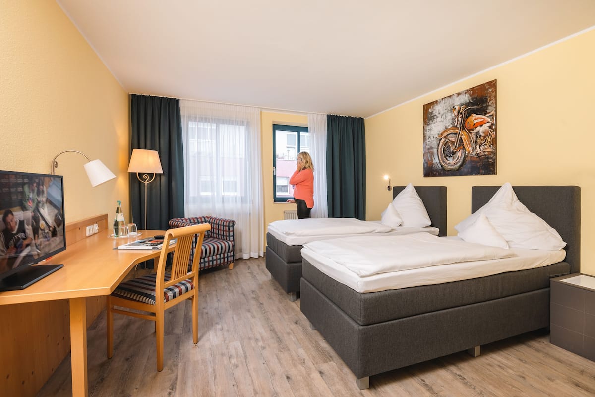 A hotel room with two beds, a desk with a computer, a chair, and a TV.