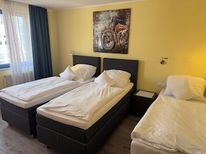A hotel room with two single beds, a nightstand, a wall-mounted painting, and a window with curtains. - Hotel am Park (Hueckelhoven)