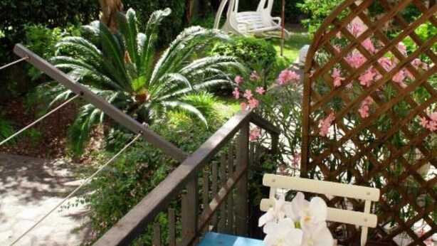 Ein Balkon mit einem blauen Tisch, einem weißen Stuhl und einem Hängesessel unter einem weißen Sonnenschirm.