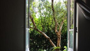 Ein Zimmer mit großem Fenster und Blick auf Bäume und Grün.