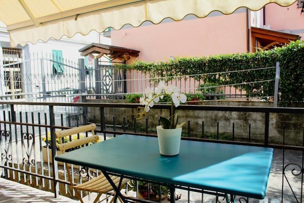 Un balcon avec une table et des chaises, un pot de fleurs et une rambarde.