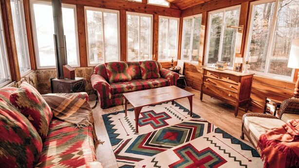 L’intérieur chaleureux d’un chalet comprend un canapé, une table basse, une commode et une grande fenêtre offrant une vue sur la forêt.