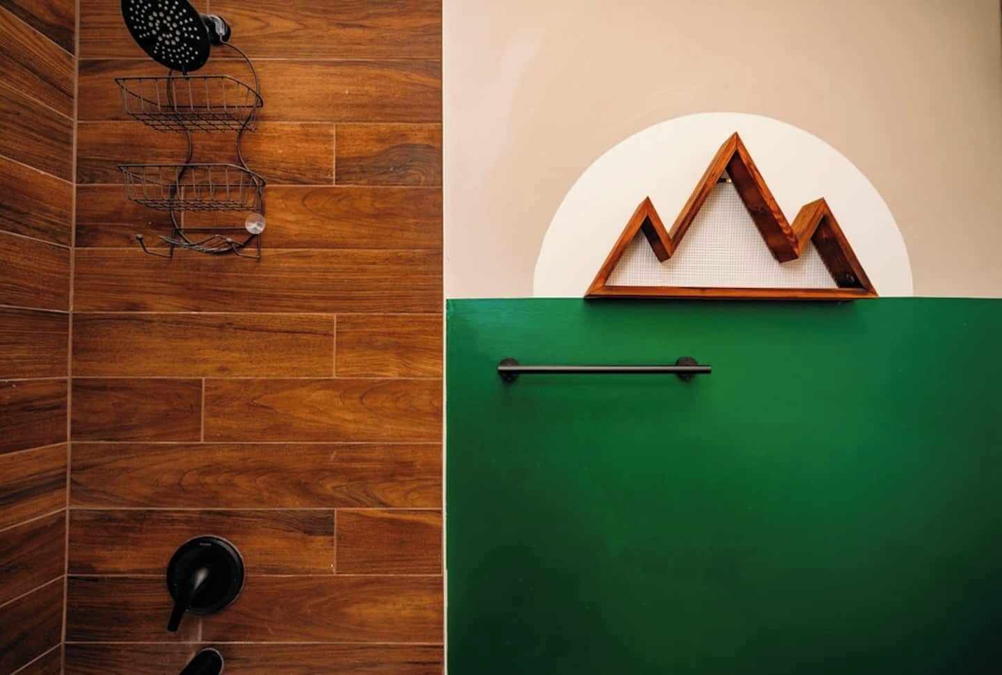 A bathroom with wooden tiles, a shower head, a towel rack, and a green wall with a geometric design.