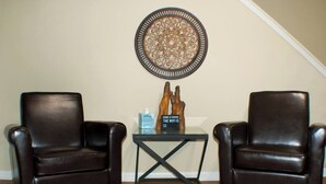 Duas poltronas de couro, uma mesa de centro de vidro com um objeto decorativo e uma caixa, e uma obra de arte na parede.