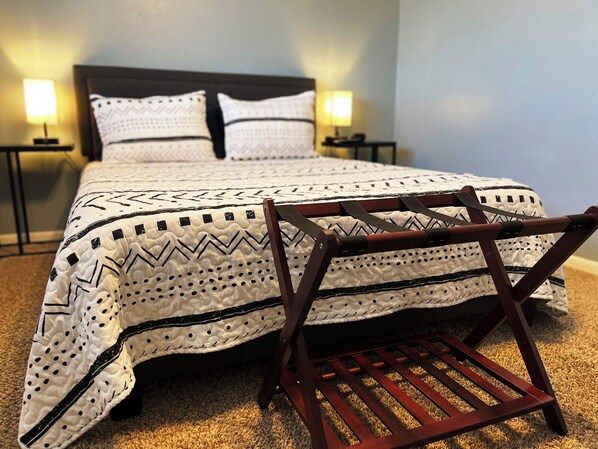 A neatly made bed with a patterned bedspread and pillows, a wooden chair, and two bedside lamps.