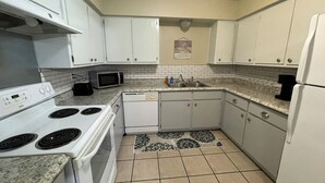 Une cuisine avec des meubles blancs, un four à micro-ondes, une cuisinière, un lave-vaisselle et un réfrigérateur.