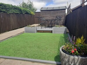 Enjoy a serene outdoor space with a lush lawn, a charming wooden structure, and a vibrant planter.