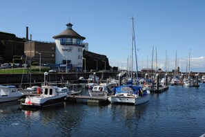 Enjoy waterfront views of the marina with boats docked in calm waters, surrounded by a historic fortification and a grassy field.