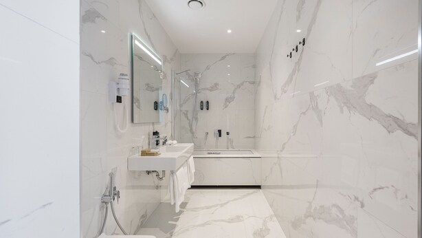 Un baño moderno con paredes de mármol, un espejo grande, un lavamanos y una zona de ducha.