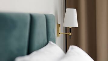 A modern hotel room with a teal upholstered headboard, a gold-framed wall-mounted lamp, and white bedding.