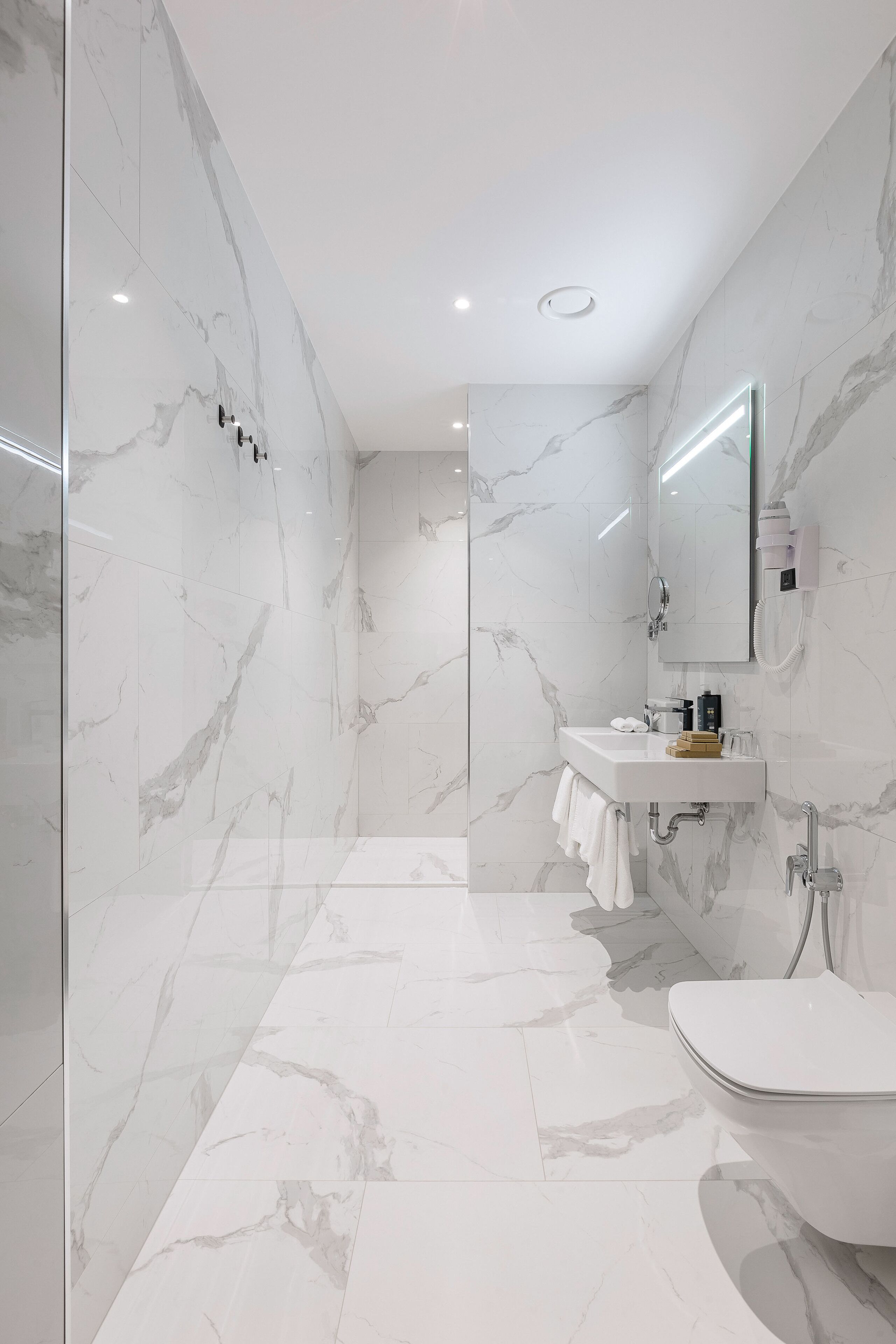 Une salle de bain moderne avec un sol et des murs en marbre, un lavabo blanc et des toilettes.