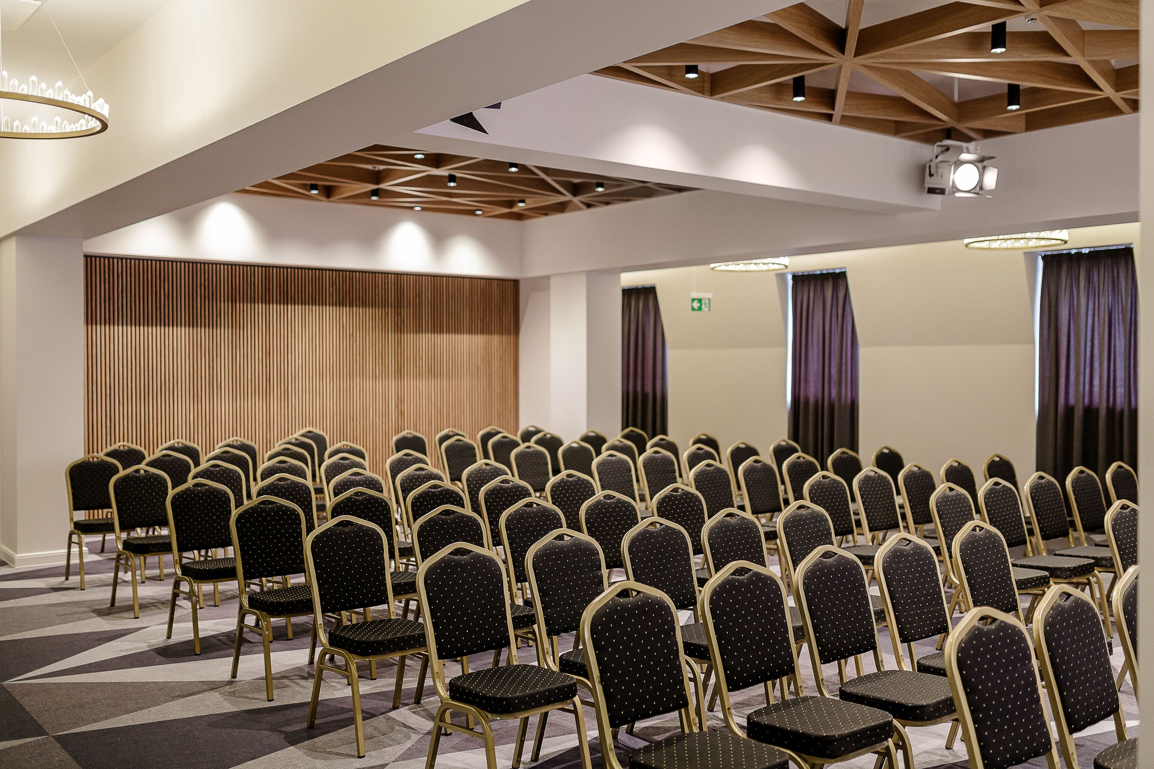 Ein Konferenzraum mit Reihen von Stühlen, einer Holzbalkendecke und einer Projektionsleinwand.