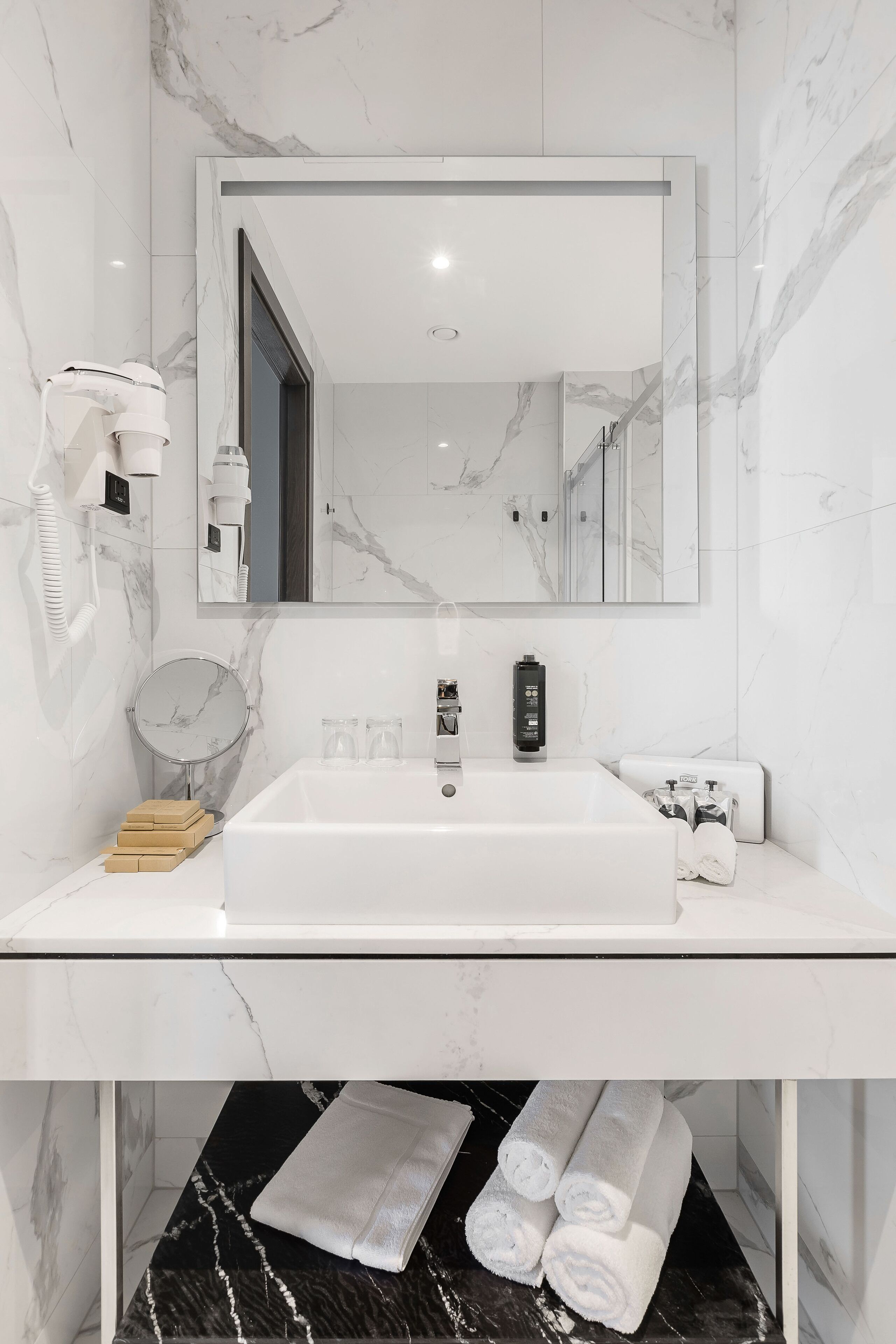 A modern bathroom with a large mirror, white sink, and marble walls.