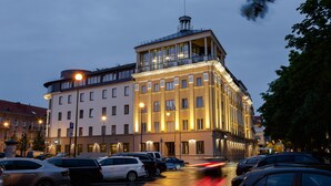 A multi-story hotel with a corner tower, large windows, and a parking lot with cars. - VICTORIA Hotel Klaipėda (Klaipeda)