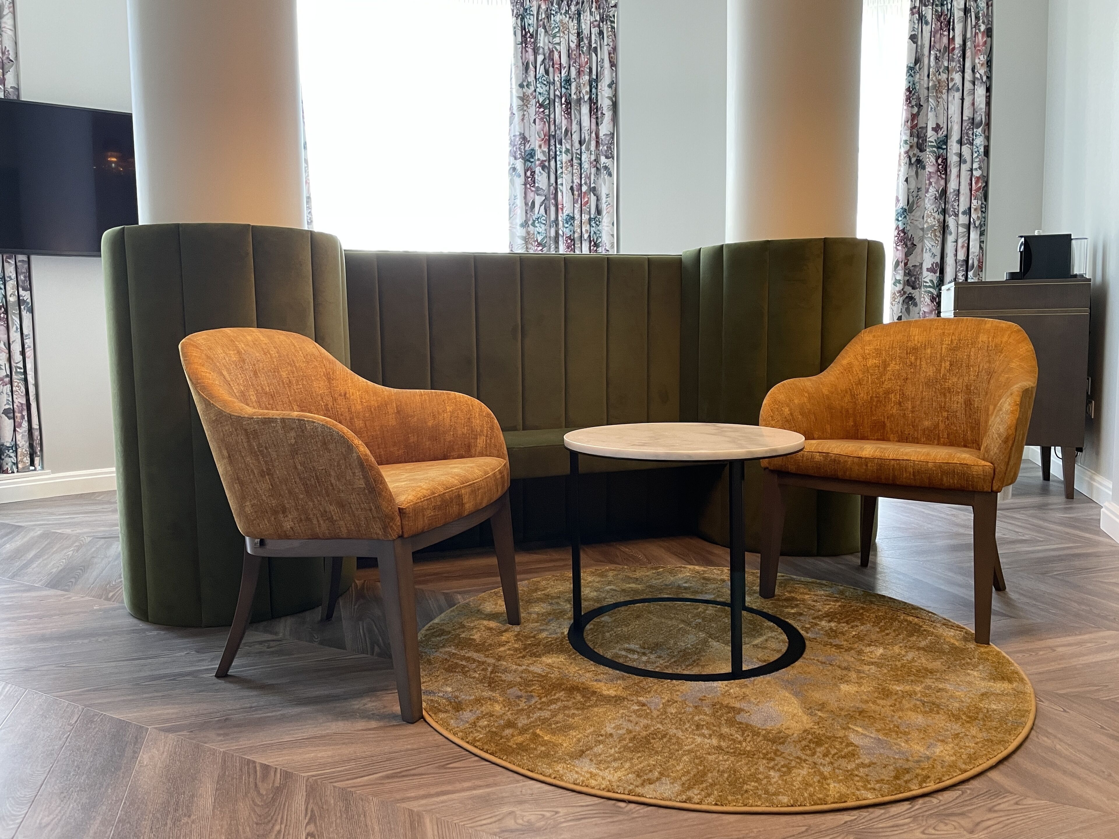 A modern living room with a green sofa, two orange armchairs, a round coffee table, and a patterned rug.