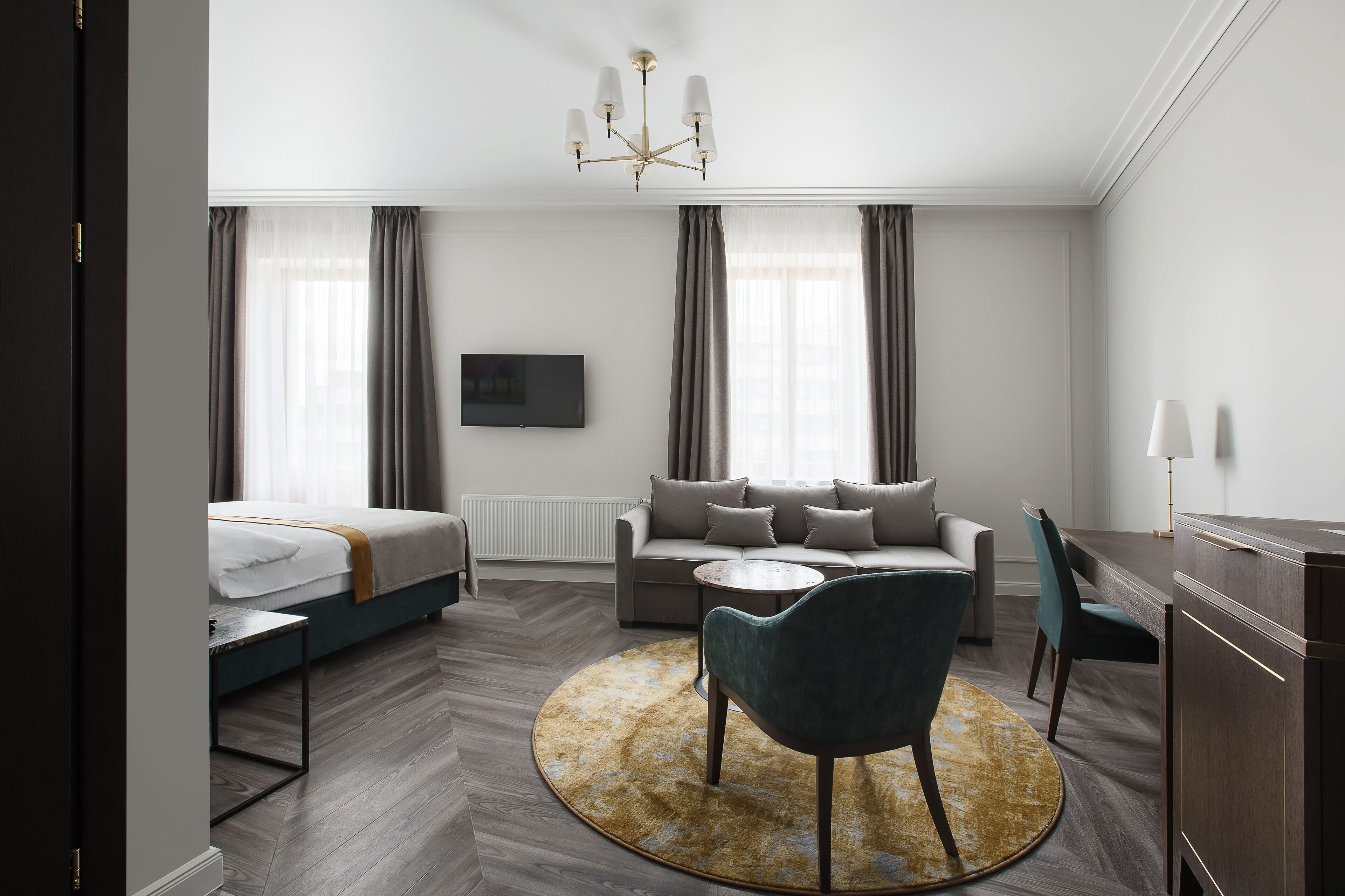 A modern hotel room with a bed, sofa, dining table, and a round rug.