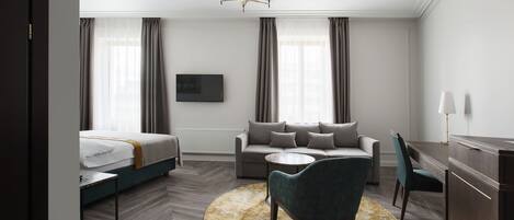 A modern hotel room with a bed, sofa, dining table, and a round rug.