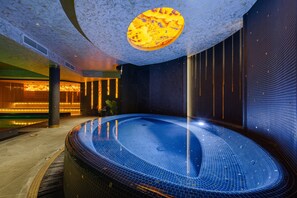 Una piscina interior moderna con un diseño de techo único, rodeada de paredes de azulejos oscuros e iluminación ambiental cálida.