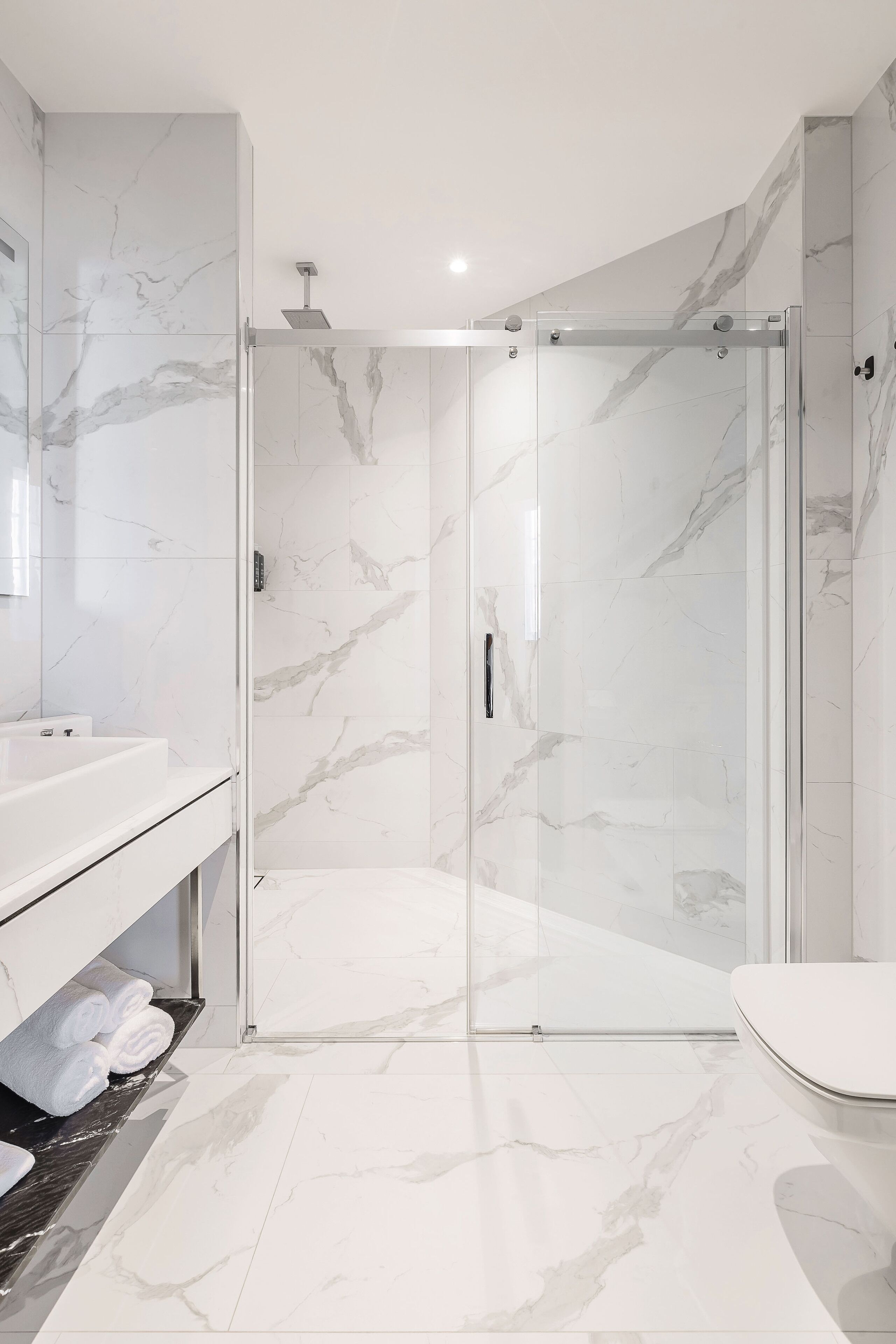 A modern bathroom with a glass-enclosed shower, a white sink, and a toilet.