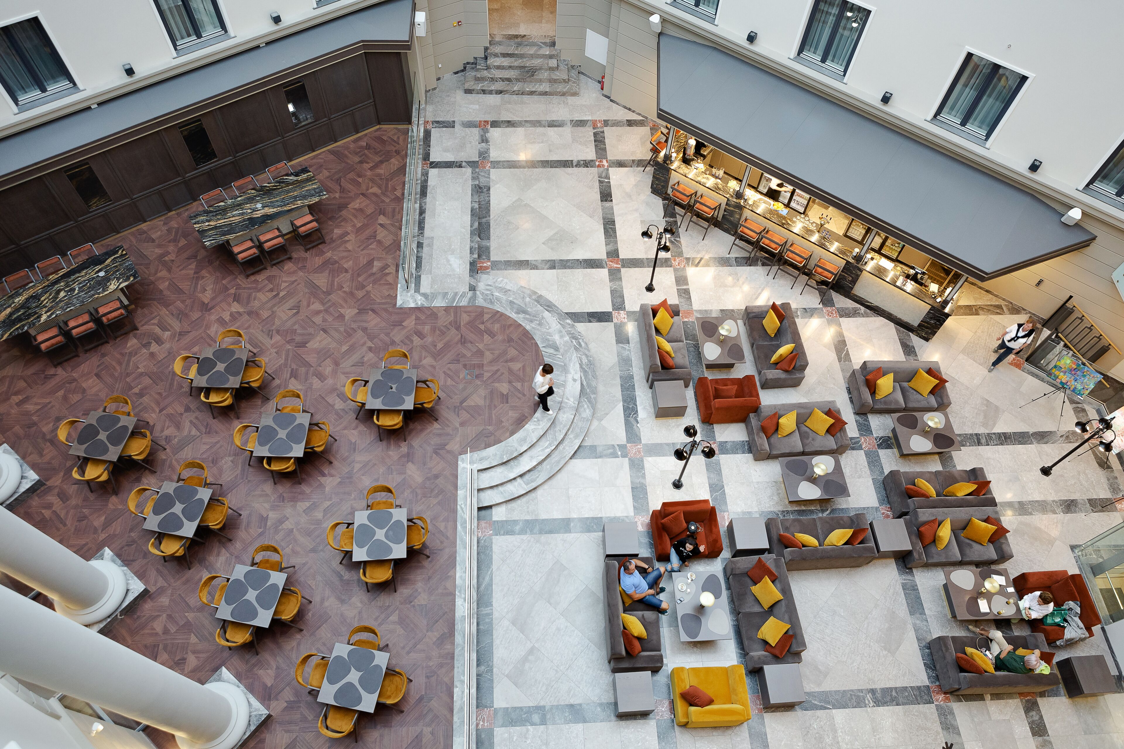 Un'ampia hall d'albergo con diverse zone relax, una scalinata centrale e un'area bar/lounge.