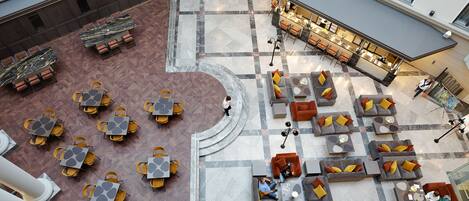Un'ampia hall d'albergo con diverse zone relax, una scalinata centrale e un'area bar/lounge.