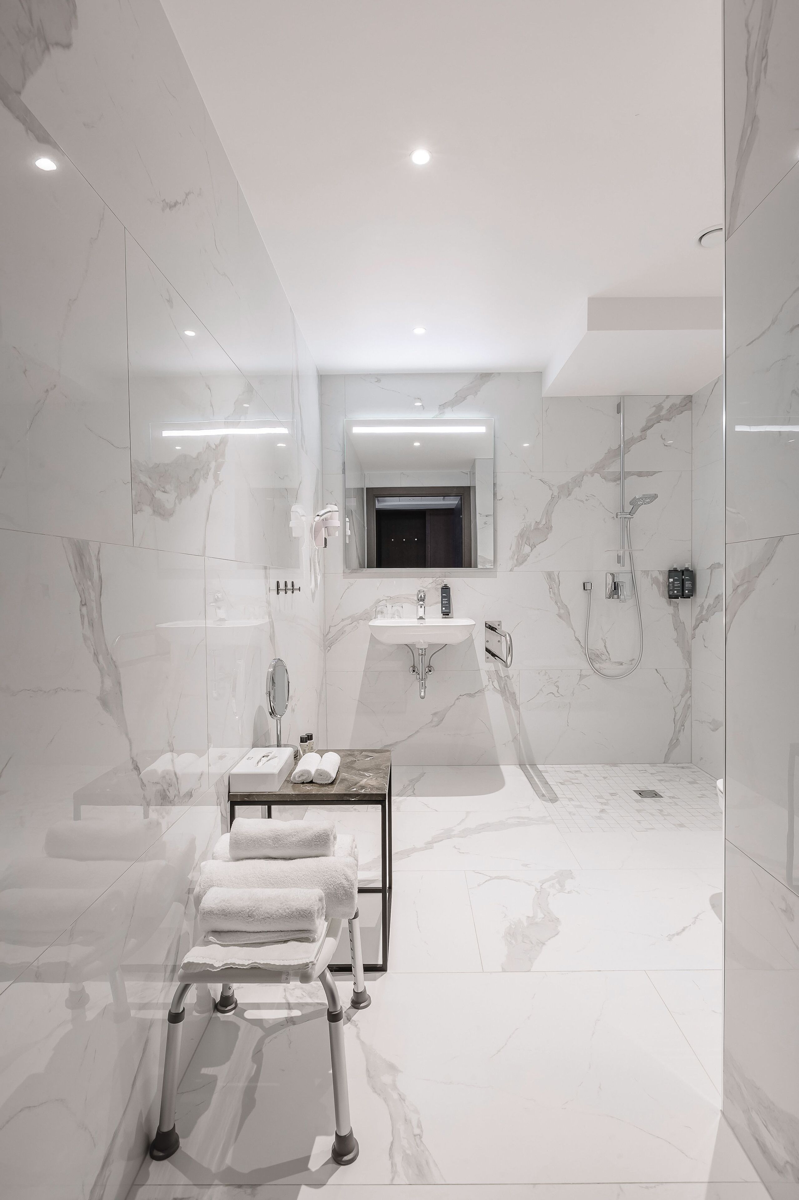 A modern bathroom with a marble floor, a glass shower enclosure, a vanity with a mirror, and a towel rack.