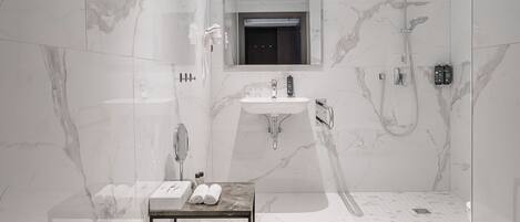 A modern bathroom with a marble floor, a glass shower enclosure, a vanity with a mirror, and a towel rack.