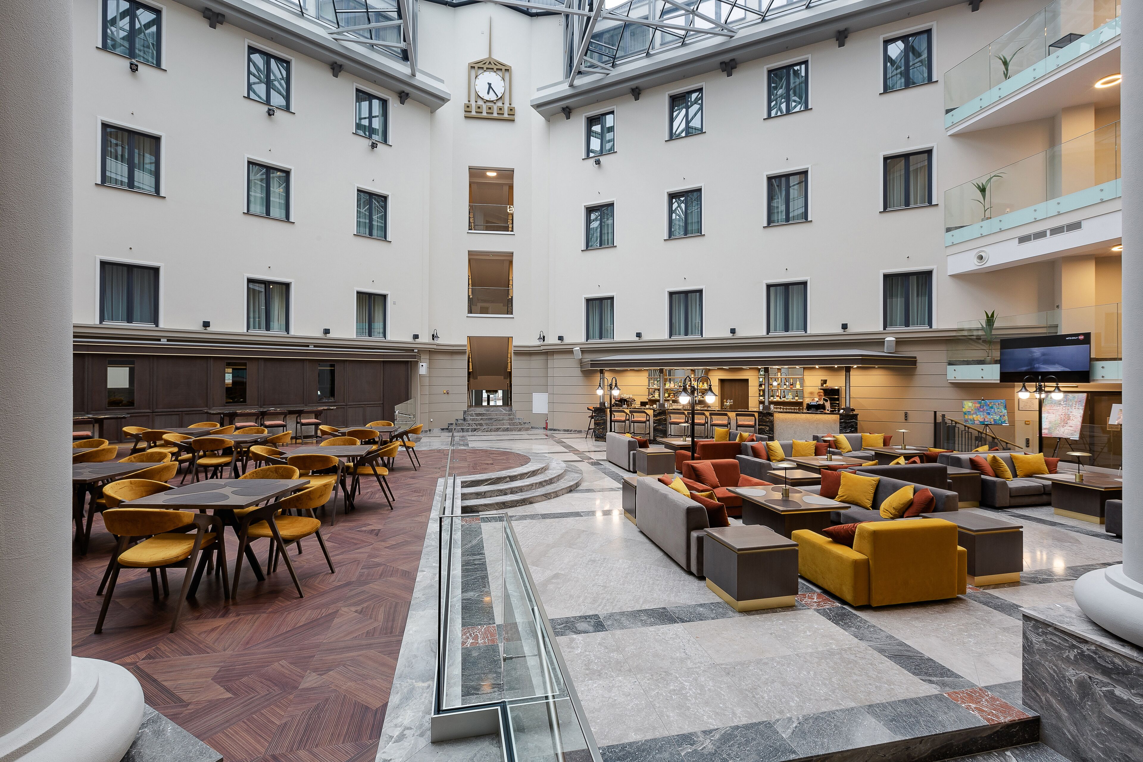 A spacious lobby with multiple seating areas, a central staircase, and a bar/lounge area.