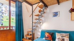 A room with a blue sofa, a spiral staircase, and a view of a residential area. - Rond Point des Pistes (Val Claret) by Interhome (Tignes)