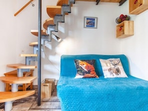 Een compacte kamer met een blauw bed, een houten trap en een klein houten tafeltje.
