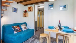 A cozy room with a blue sofa, wooden ceiling beams, a dining table with blue plates, and a small kitchen area. - Rond Point des Pistes (Val Claret) by Interhome (Tignes)