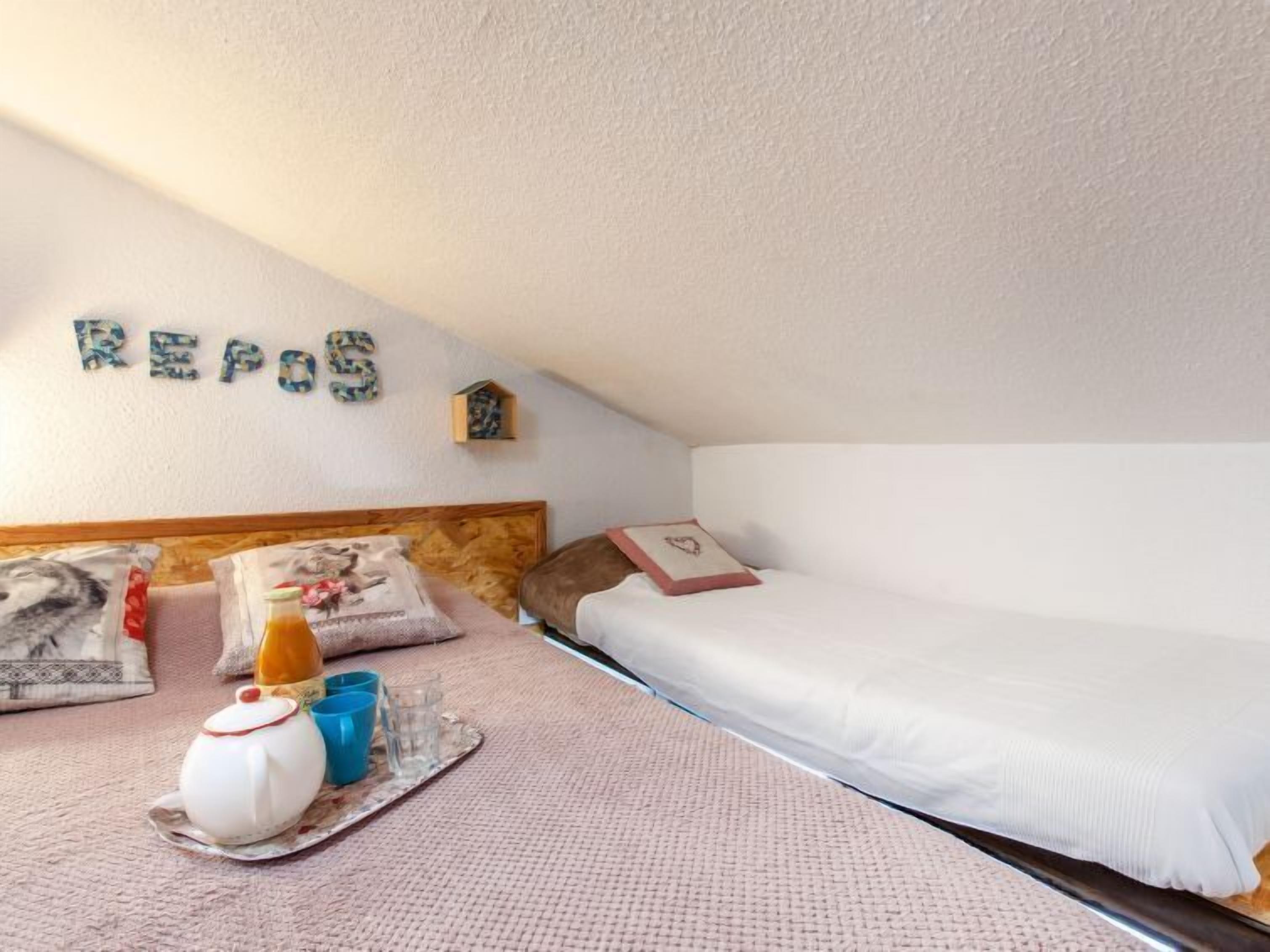 A cozy bedroom with a bed, pillows, a small shelf with a birdhouse, and a wall with the word 'REPOS' spelled out.