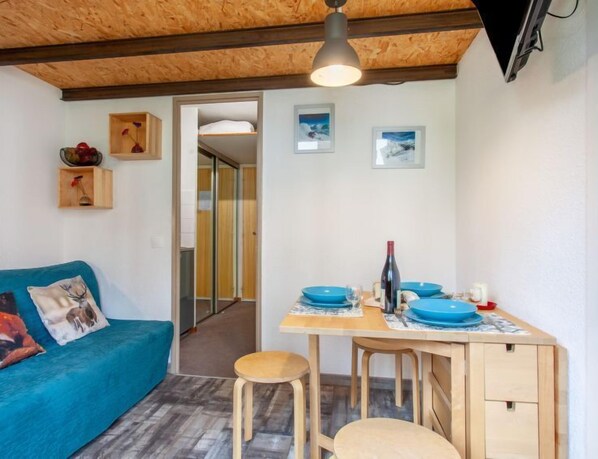 A cozy room with a wooden ceiling, a blue sofa, a small dining table with blue plates, and a bottle of wine. - Rond Point des Pistes (Val Claret) by Interhome (Tignes)