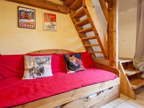 Un lit superposé en bois avec un matelas rouge et deux oreillers, l’un décoré d’un cerf et l’autre d’un renard. Deux affiches sont accrochées au mur au-dessus du lit.