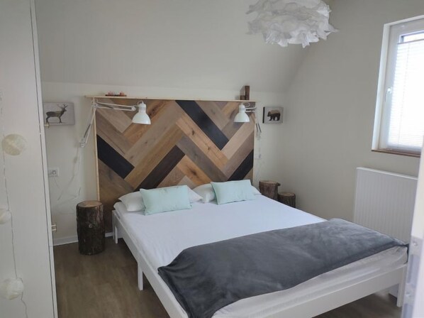 A bedroom with a wooden herringbone headboard, a bed with white and grey bedding, two bedside lamps, and a small shelf with decorative items. - Waldoase by Interhome (Bad Arolsen)