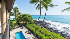 A balcony with a pool, palm trees, and a view of the ocean.