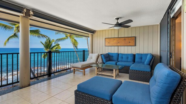 A balcony with a view of the ocean, a blue sofa, and a glass table.