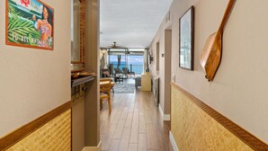 A hallway with a wooden floor, a dining area with a table and chairs, a ceiling fan, and a view of the ocean.