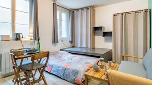 A compact living space with a bed, a small table, a chair, and a kitchenette area. - Le studio St Vincent by Interhome (Saint Malo)