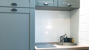 A modern kitchen with grey cabinets, a white tiled backsplash, and a stainless steel sink. - Le studio St Vincent by Interhome (Saint Malo)