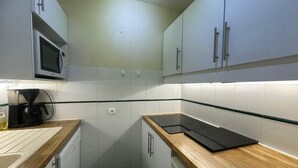 A compact kitchen with white cabinets, a microwave, a coffee maker, and a black induction cooktop. - 100m from ski slopes, 6th floor, view ski slopes, swimming pool, balcony, tv, ski locker, 35m² (La Plagne)