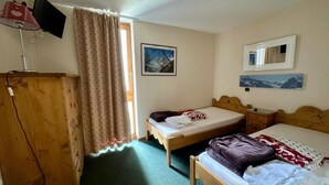 A small, cozy room with two single beds, a wooden wardrobe, a desk with a chair, and a window with curtains. - 100m from ski slopes, 6th floor, view ski slopes, swimming pool, balcony, tv, ski locker, 35m² (La Plagne)